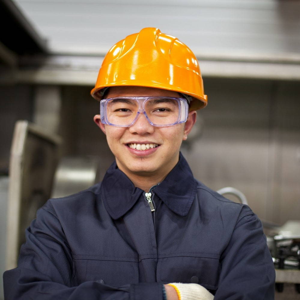 Image of a man wearing a yellow hard hat and safety glasses, smiling