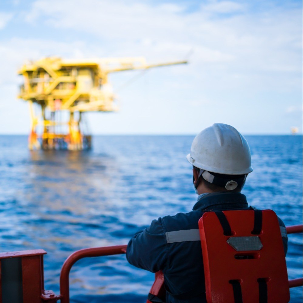 Engineer in PPE overlooking offshore oil and gas wellhead platform at sea