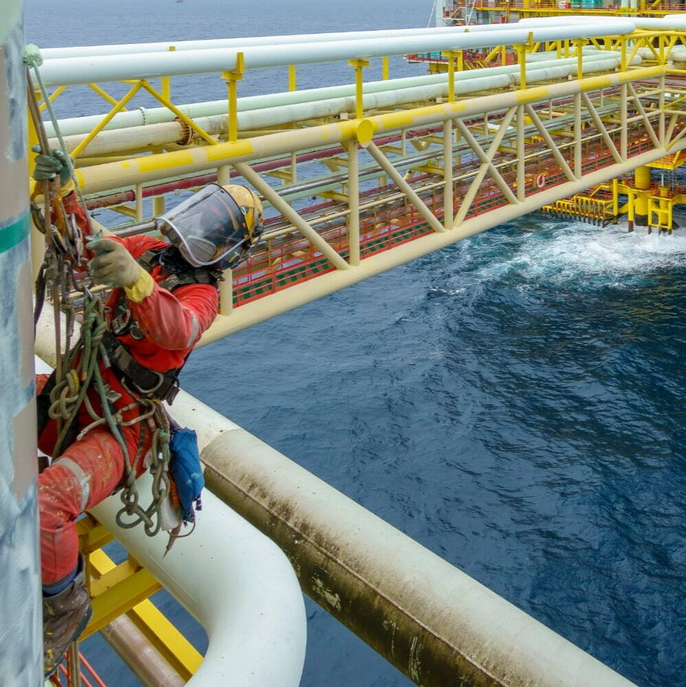 Abseiler on an offshore gas platform in PPE painting at platform edge with open sea in background